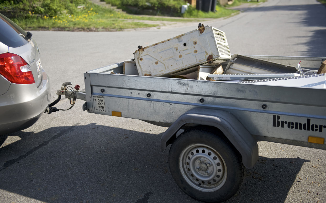 Trailer fyldt med gammelt elektronik og metaldele, tilkoblet en bil. Traileren er klar til at blive kørt til genbrugspladsen for korrekt affaldssortering og genbrug