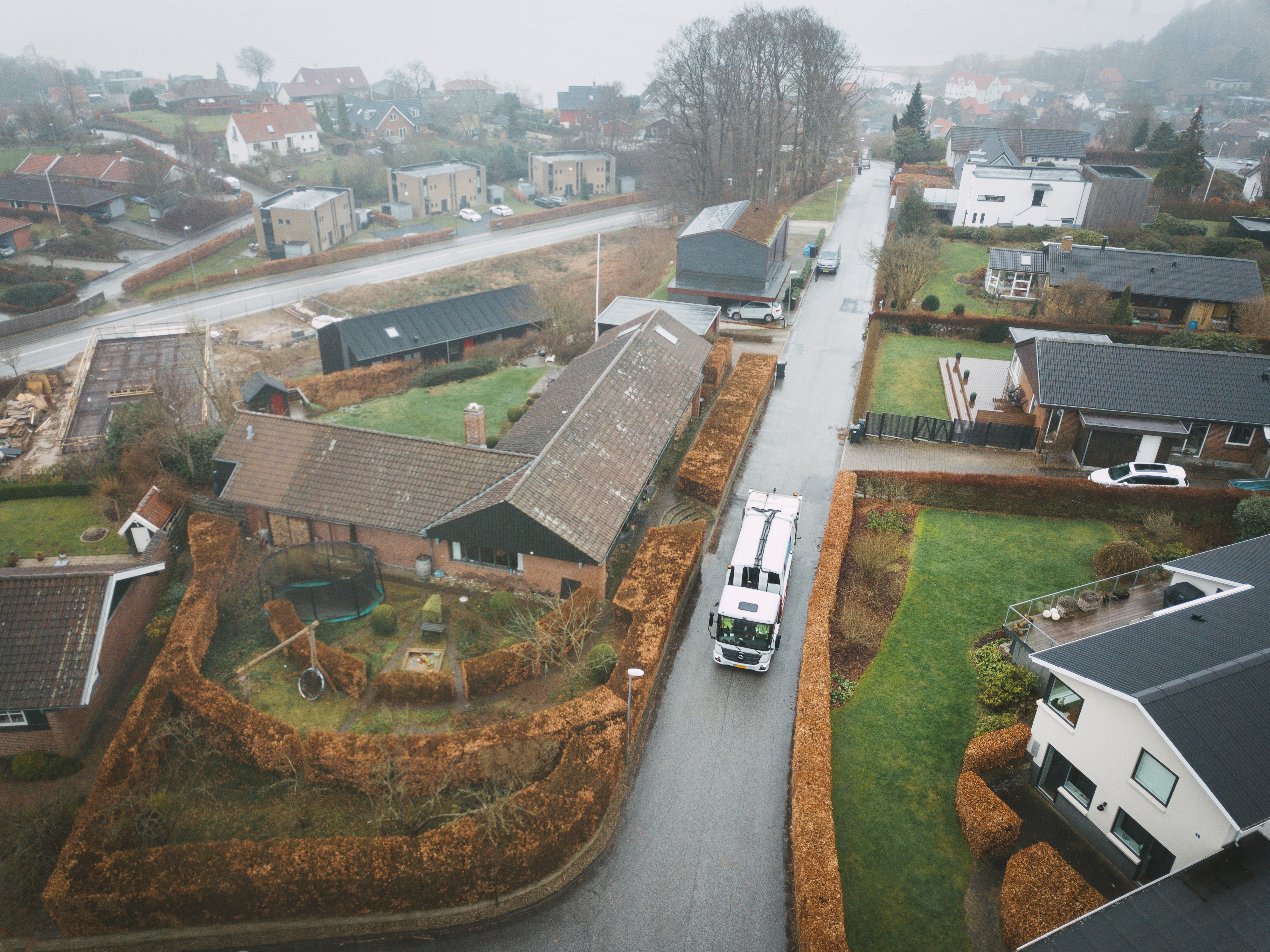 Oversigtsbillede af en affaldsindsamling i et villakvarter på en gråvejrsdag, med skraldebilen midt i arbejdet.