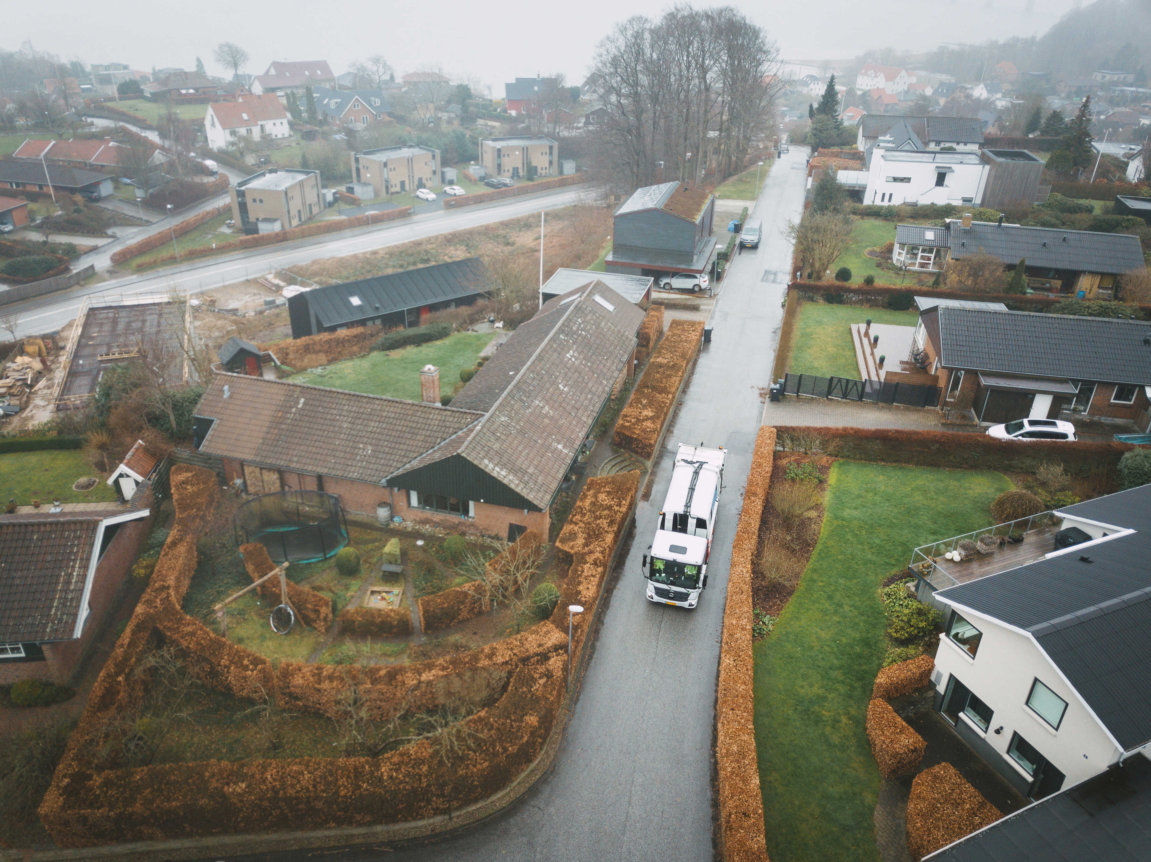 Oversigtsbillede af en affaldsindsamling i et villakvarter på en gråvejrsdag, med skraldebilen midt i arbejdet.