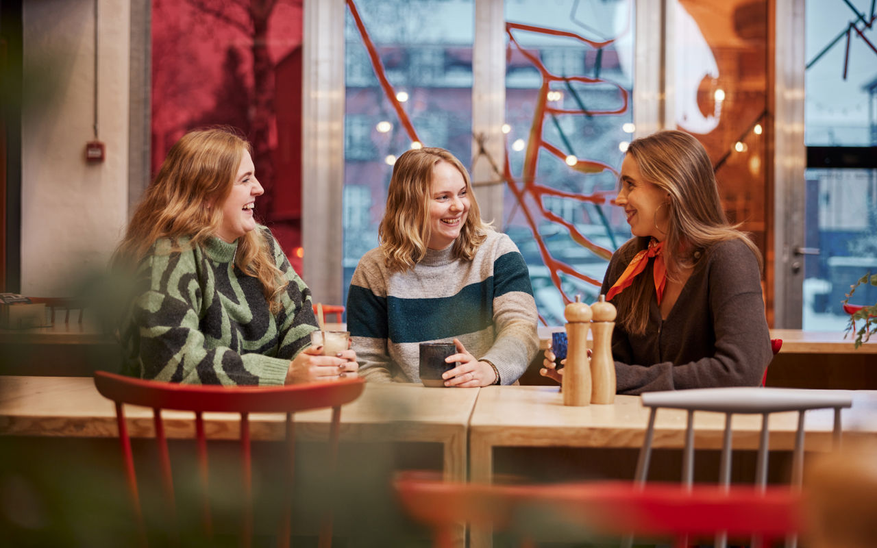 Foto af unge siddende ved et bord med kaffe/the i hænderne