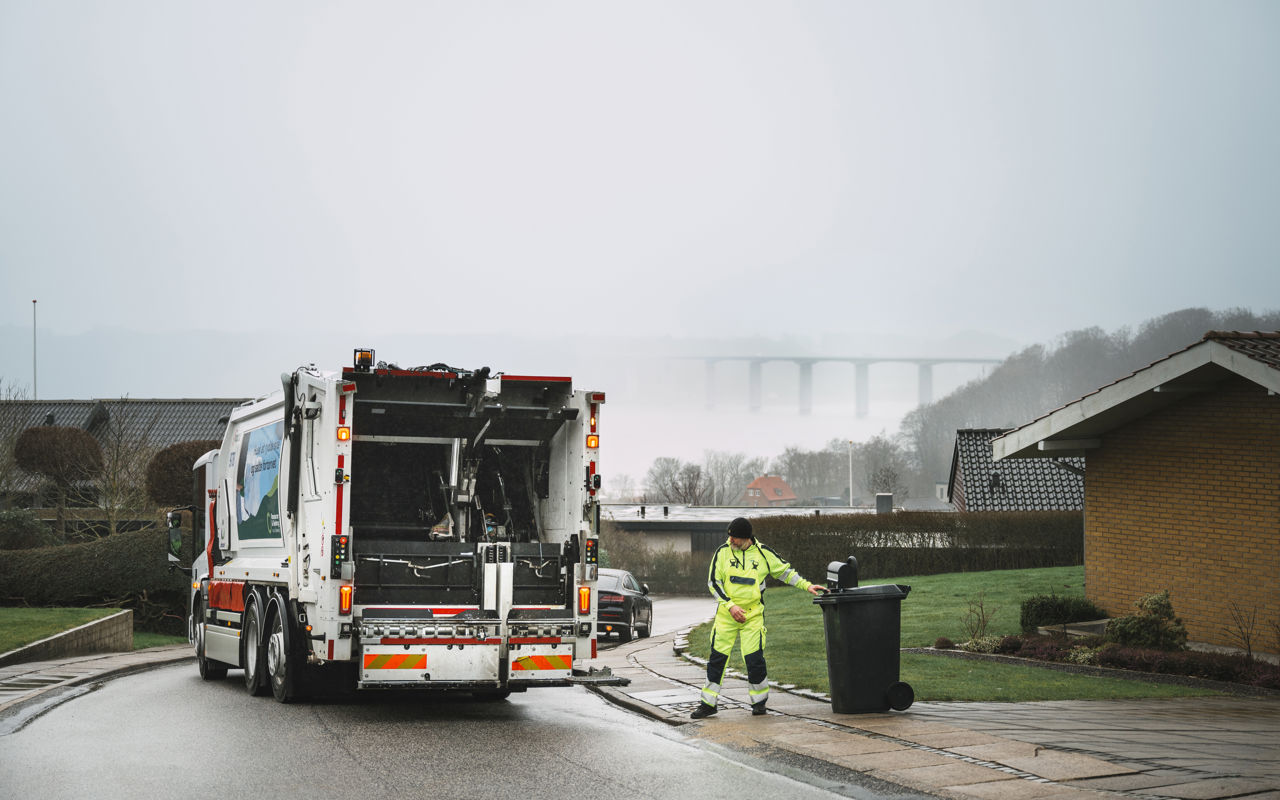 Bagenden af en skraldebil under arbejdet, med udsigt over et boligområde.